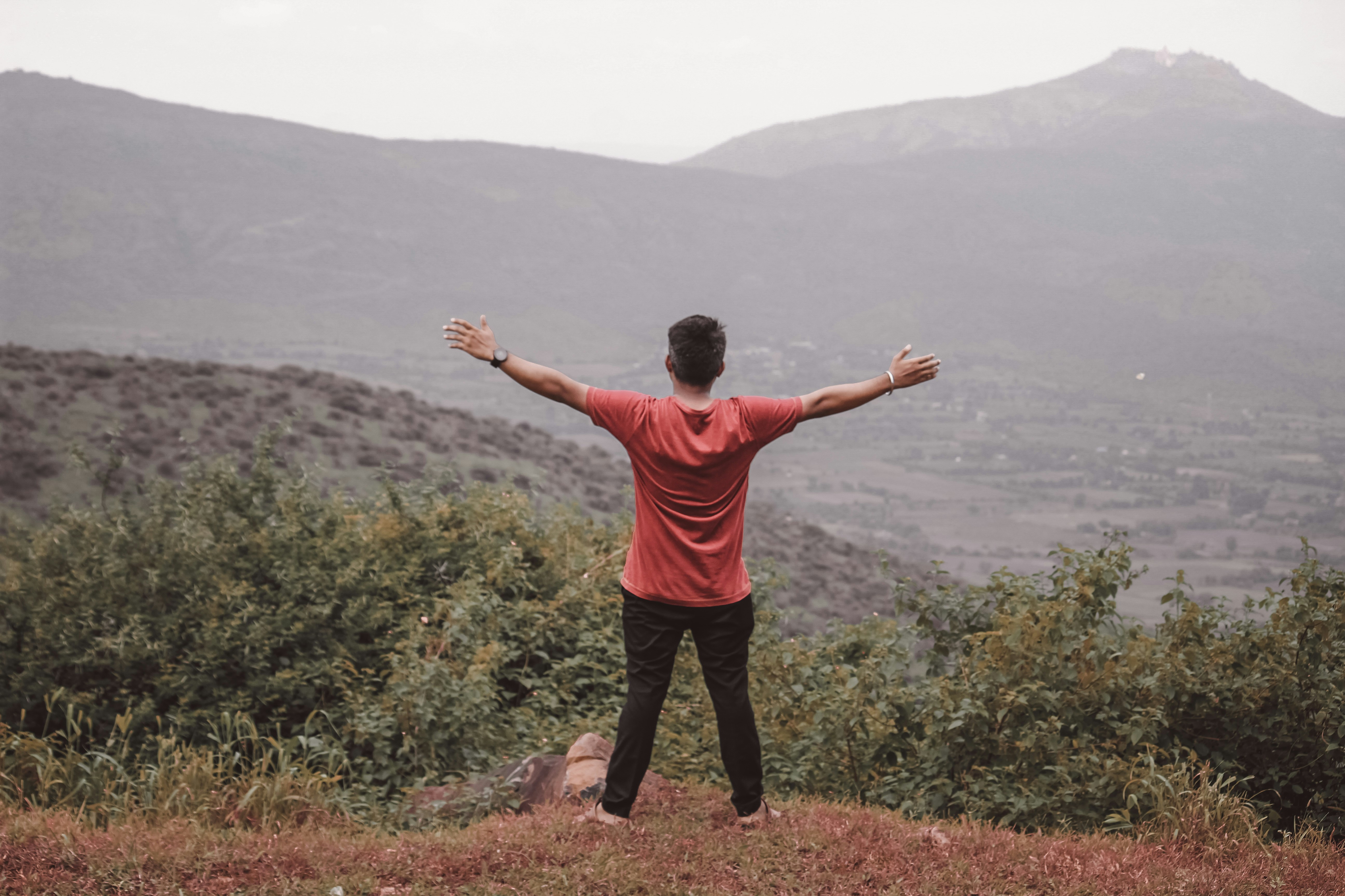 Mann steht mit ausgebreiteten Armen auf einem Hügel und blickt in eine weite Berglandschaft – Symbol für Freiheit, Selbstentwicklung und mentale Stärke