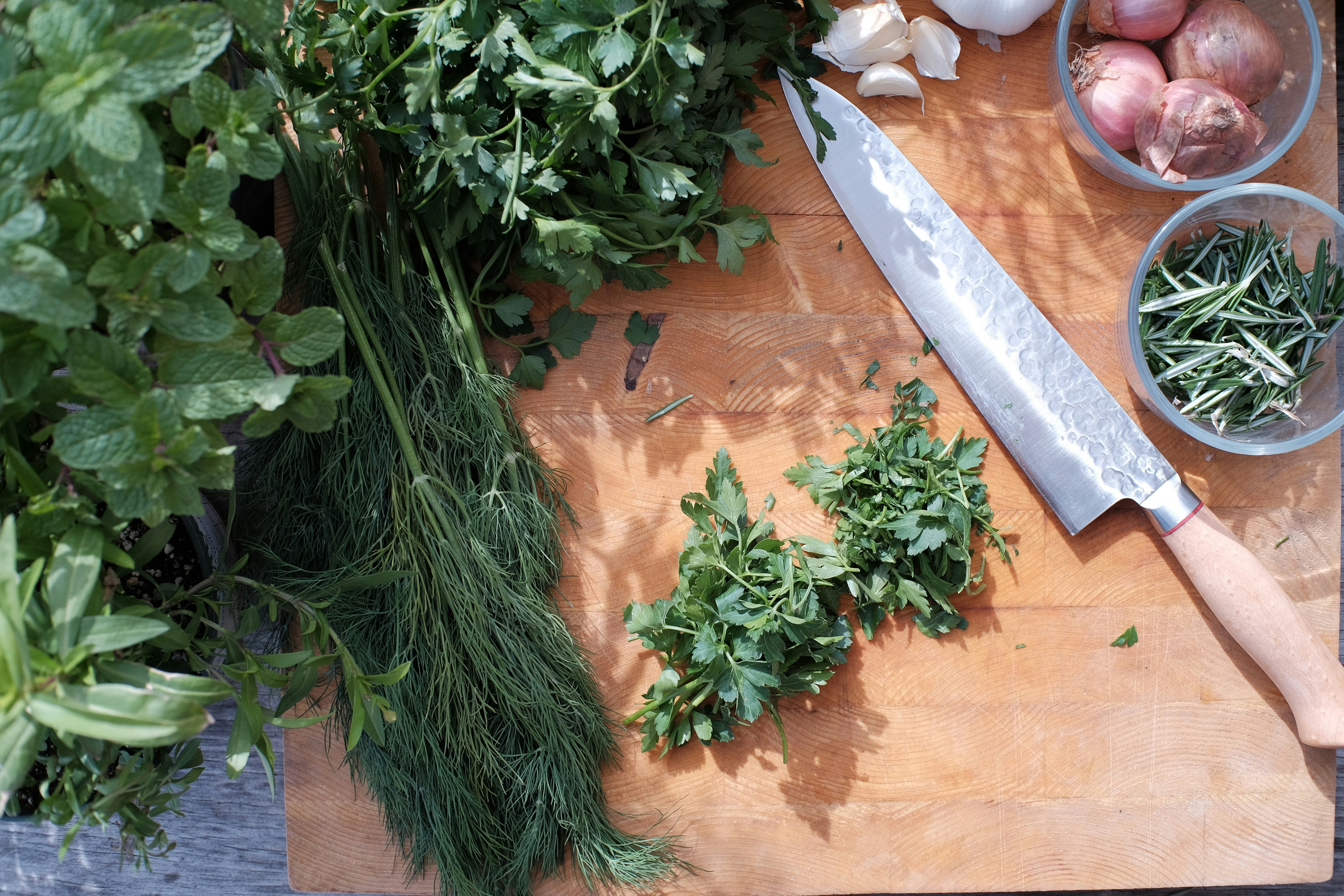 Verschiedene frische Kräuter wie Petersilie, Dill und Rosmarin liegen auf einem Holzbrett neben einem Messer und Zutaten