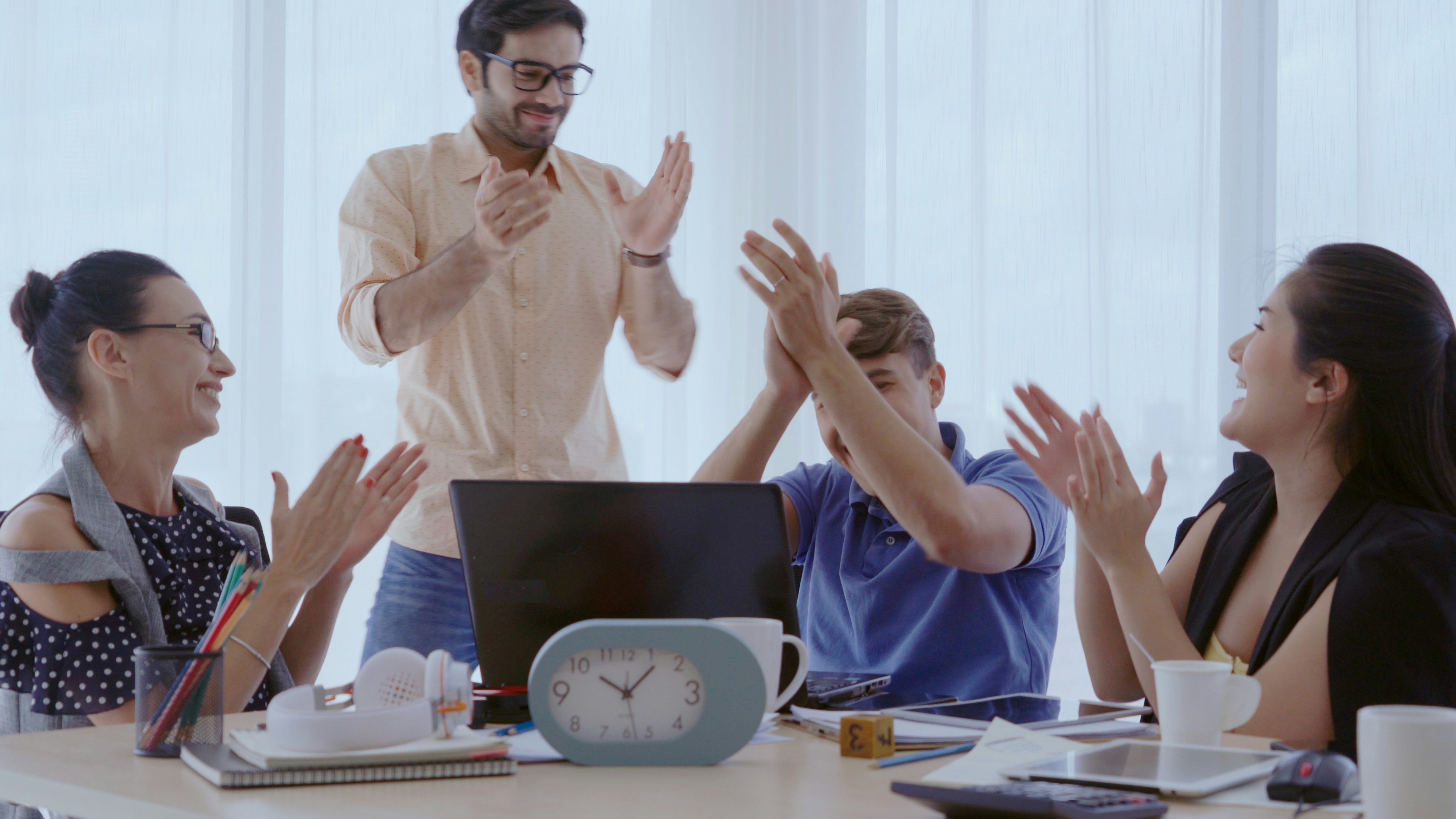 Learn@Home - Team sitzt am Tisch mit Laptop und klatscht sich ab; mehrere Personen applaudieren.