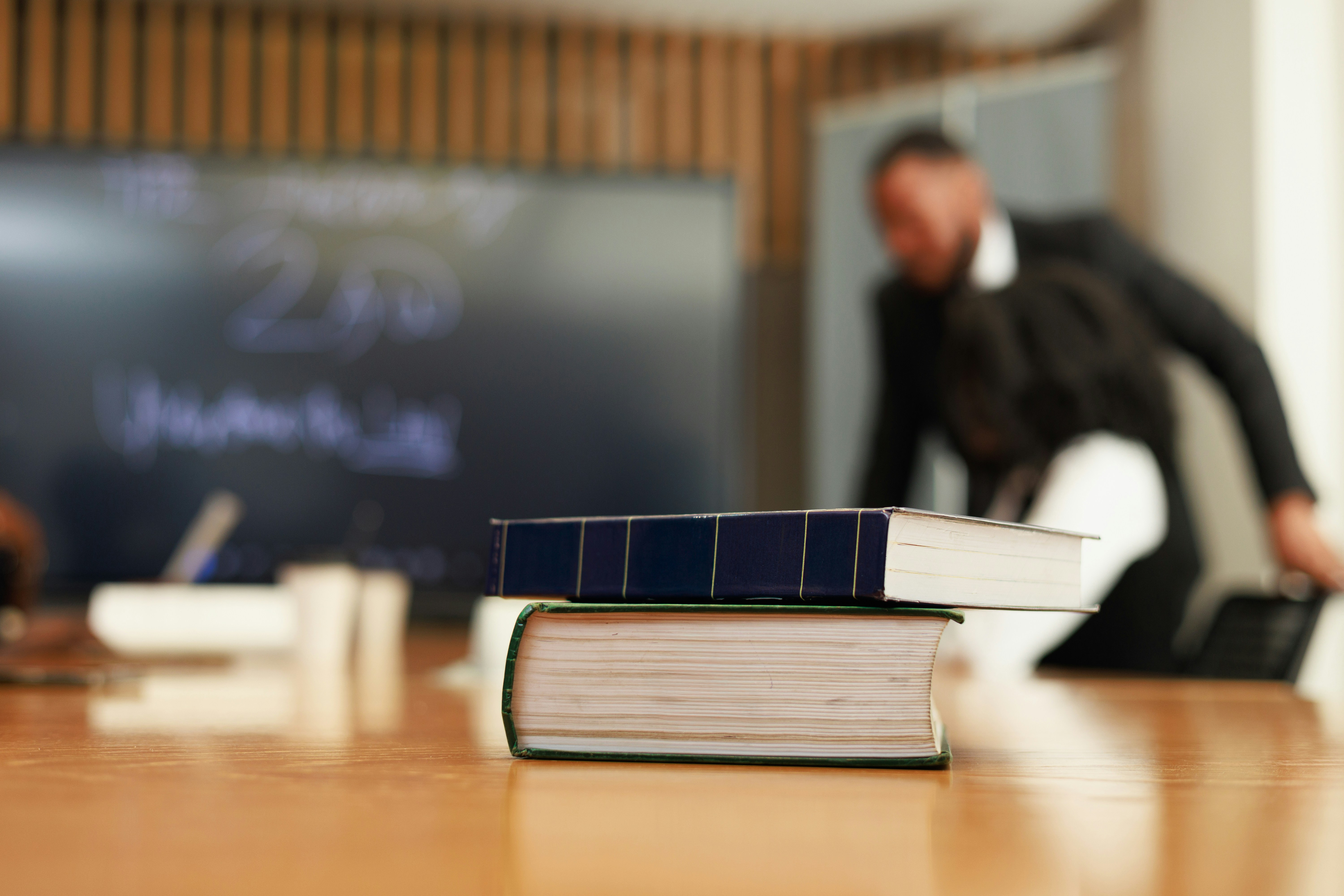 Learn@Home - Bücher im Vordergrund während einer Weiterbildung mit einem Vortragenden im Hintergrund