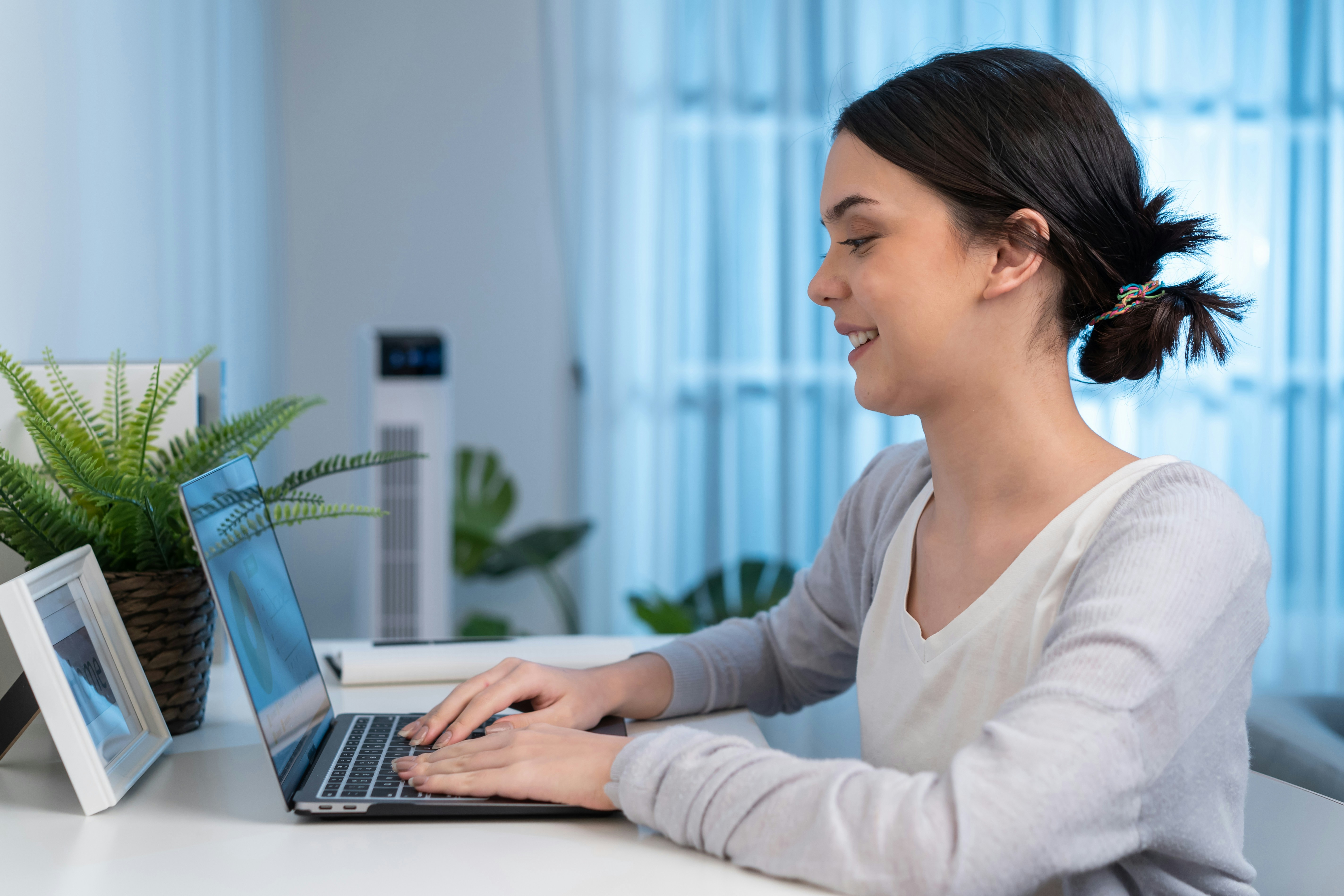 Learn@Home - Junge Frau sitzt zu Hause am Schreibtisch und lernt online mit ihrem Laptop
