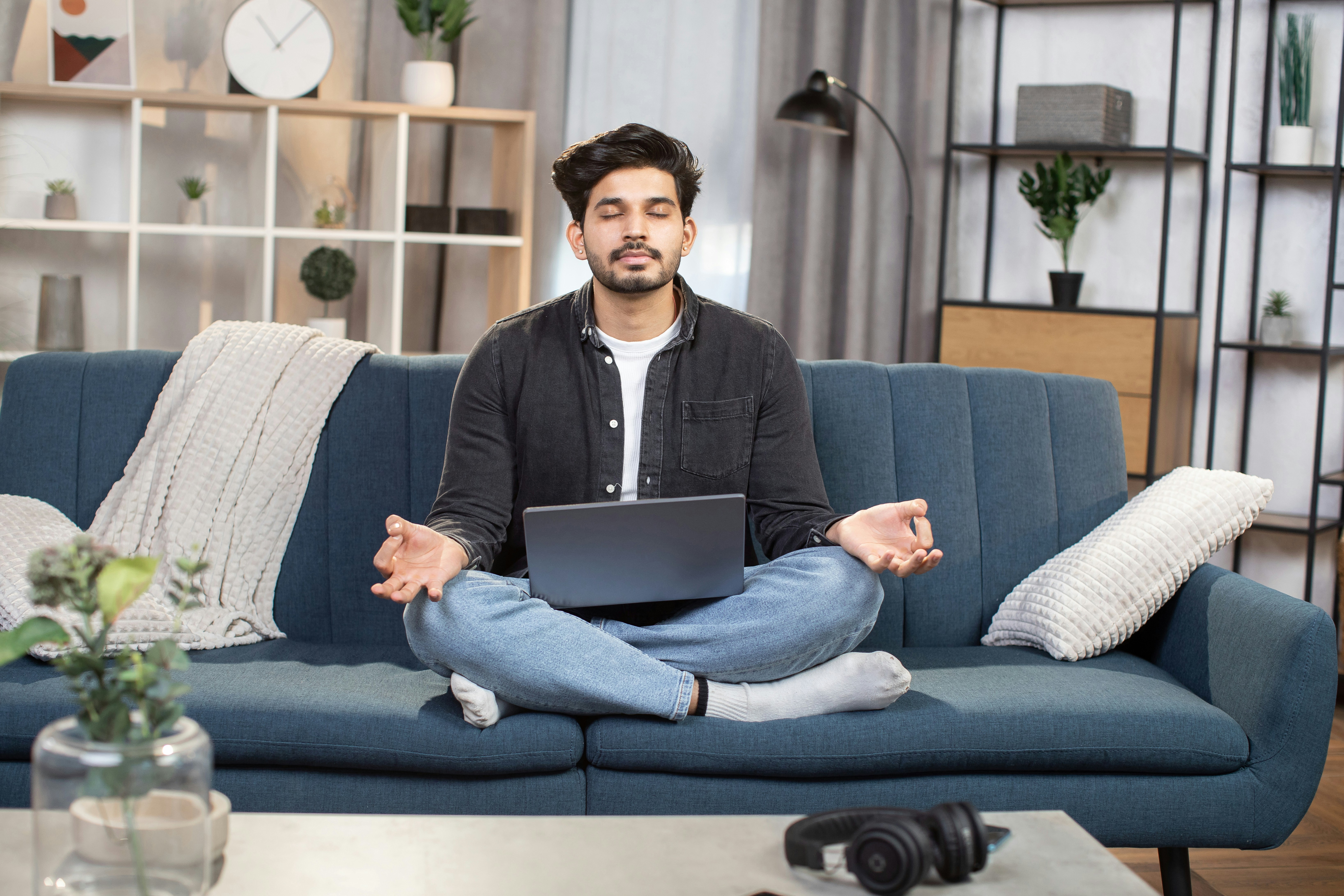 Learn@Home - Mann meditiert mit geschlossenen Augen auf einer Couch mit Laptop auf dem Schoß.