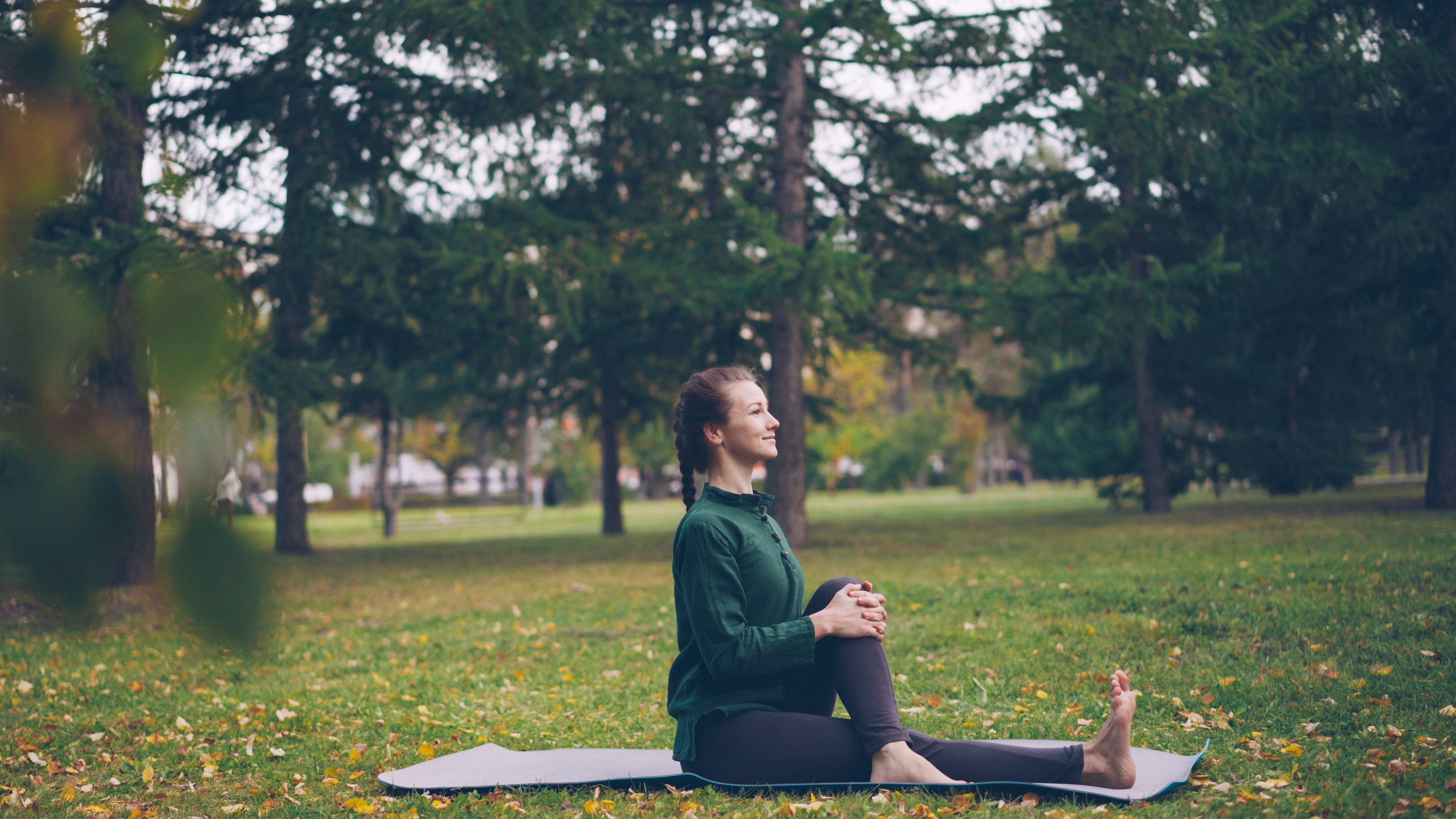 Learn@Home - Frau bei einer achtsamen Körperübung auf einer Yogamatte im Park