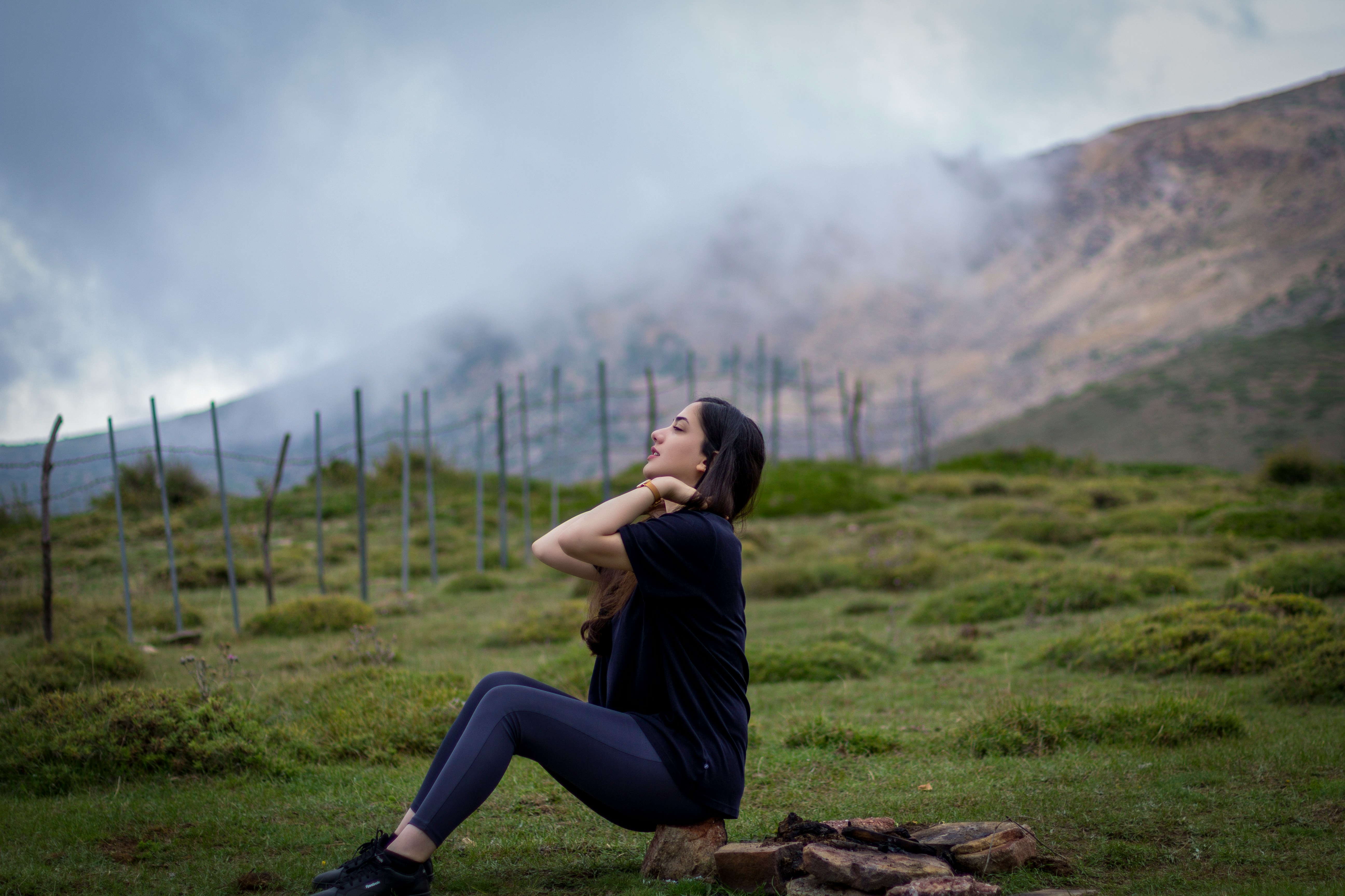 Learn@Home - Junge Frau sitzt auf einem Baumstumpf in einer grünen Berglandschaft und genießt einen ruhigen Moment in der Natur.